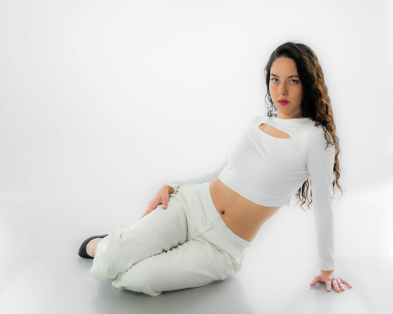 Woman posing elegantly in white clothing against a white background, showcasing modern fashion and style.