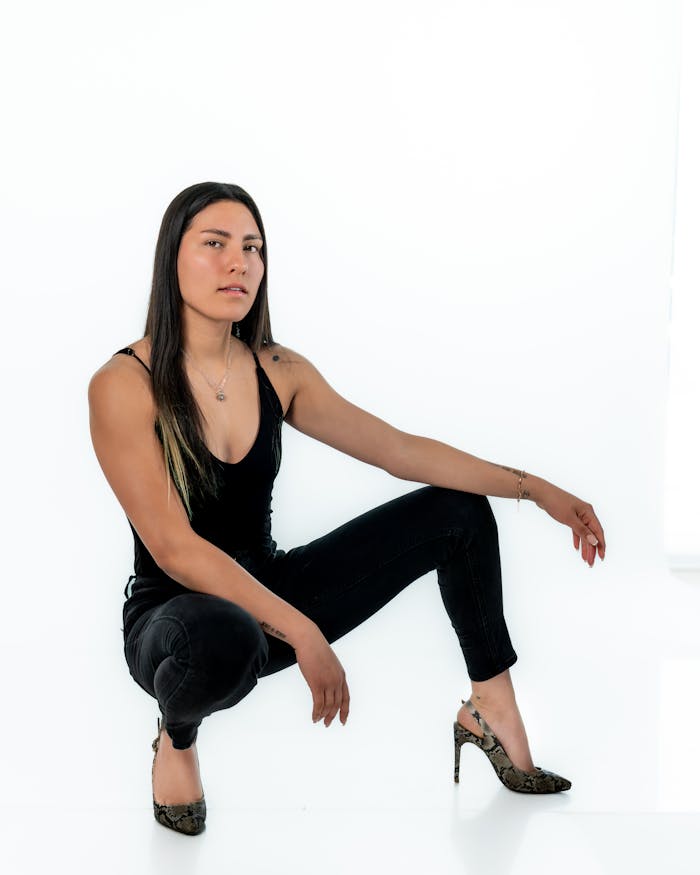 Striking pose of a stylish woman in high heels and black attire against a white background.