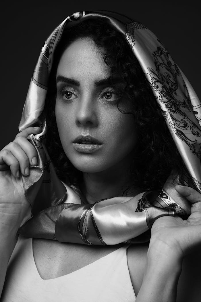 A captivating black and white portrait of a woman with a scarf draped over her head, showcasing elegance and timeless beauty.