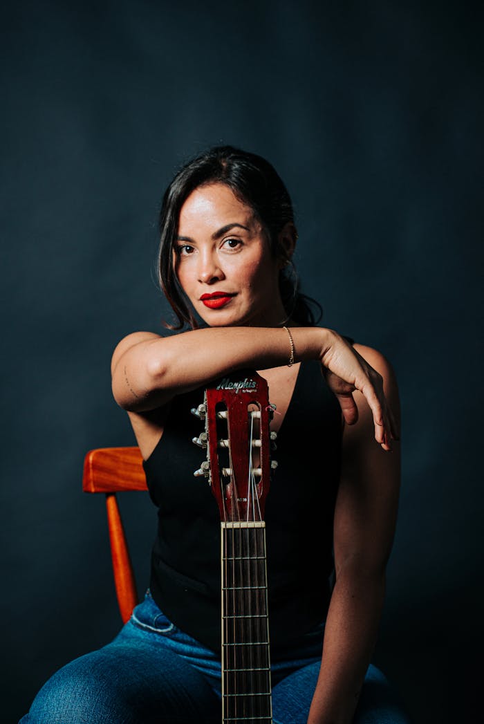 A confident woman poses with a guitar in a studio setting, showcasing modern fashion and music passion.